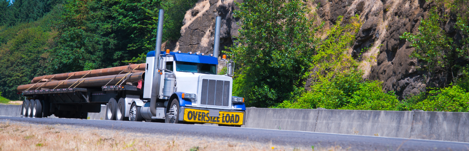 Truck transporting an oversized load of large pipes on a scenic highway