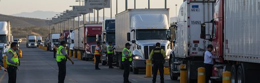 Commercial trucks lined up at a checkpoint with officers inspecting freight vehicles.