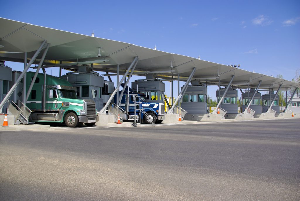 Commercial trucks passing through a customs checkpoint at the U.S. border, illustrating cross-border logistics and compliance readiness.
