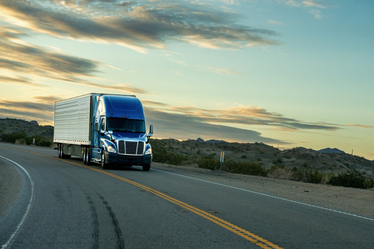 Semi-truck driving on an open highway at sunset, representing the speed and urgency of expedited shipping.