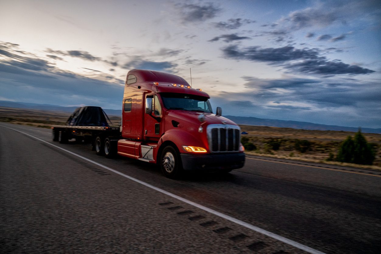 Oversize load semi-truck transporting heavy construction equipment on a lowboy trailer along a rural highway.