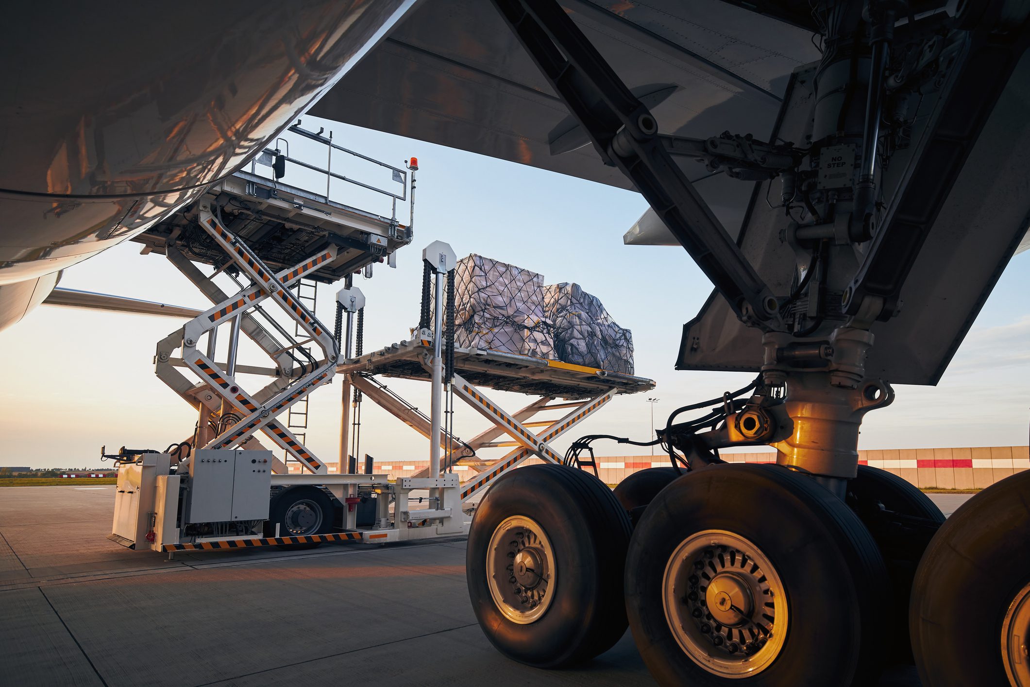 Palletized cargo wrapped in netting elevated on a scissor lift for loading into an aircraft during air freight operations.