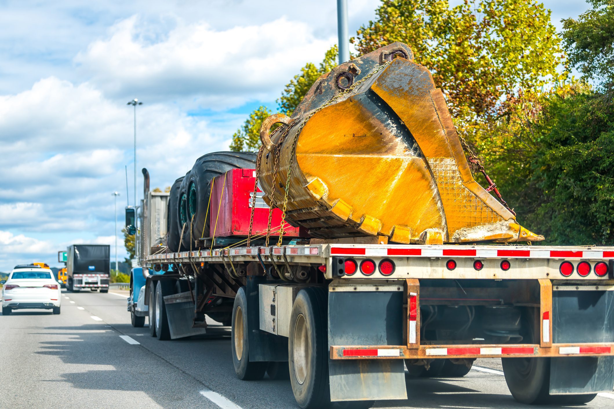 Oversize load semi-truck transporting heavy construction equipment on a lowboy trailer along a rural highway.