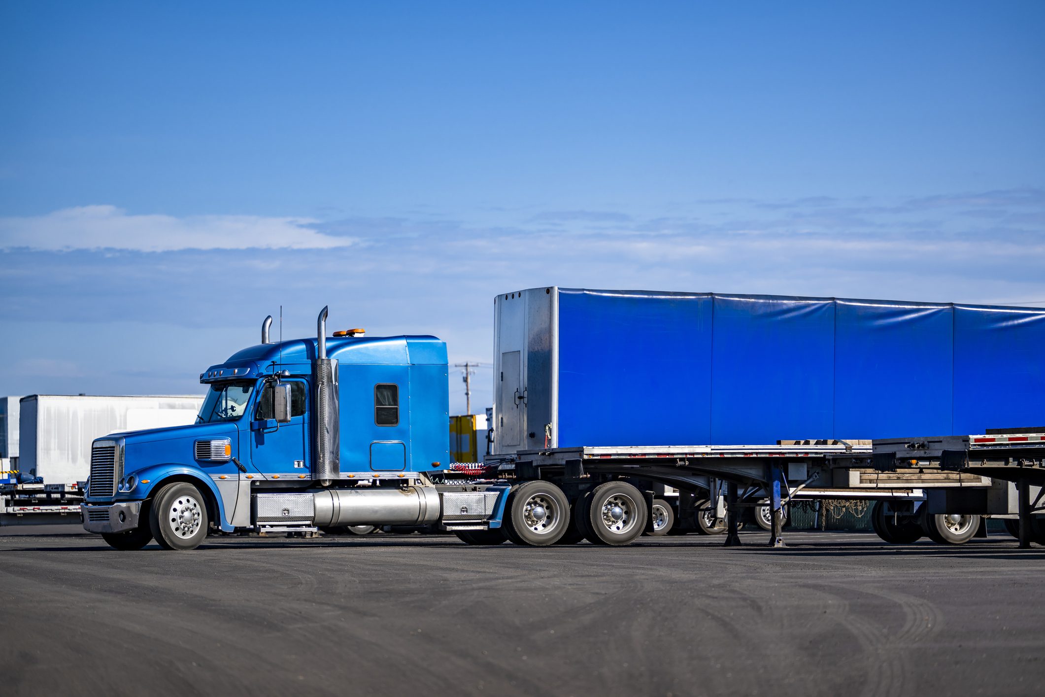 Conestoga trailer with fully enclosed tarp system preparing to depart a freight yard under clear skies.