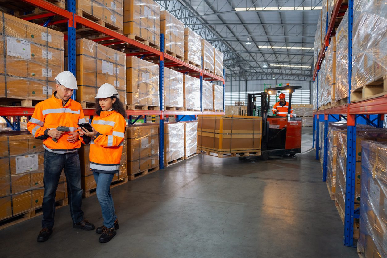 Logistics professionals in high-visibility safety gear managing inventory in a warehouse ensuring safe and efficient Conestoga shipping.