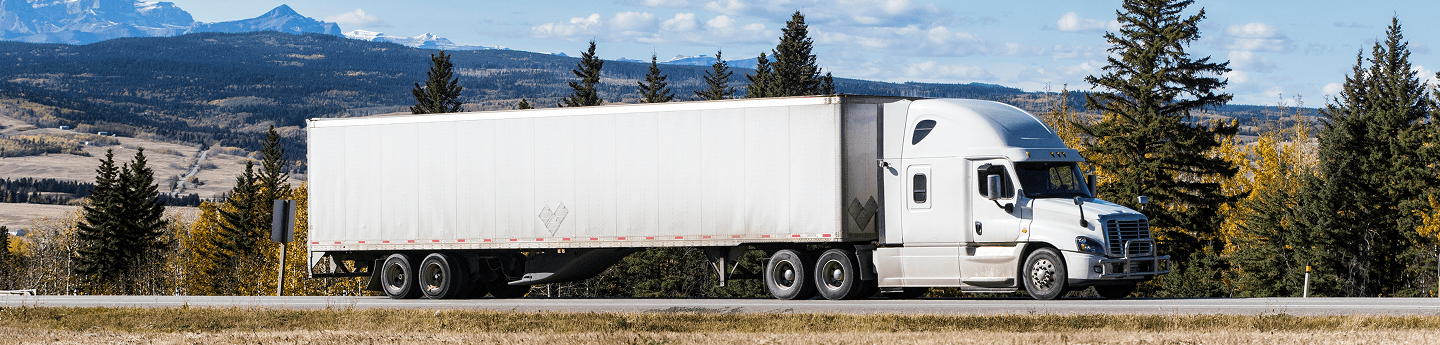 A truck driving on a highway beside a forested shoreline and mountains.