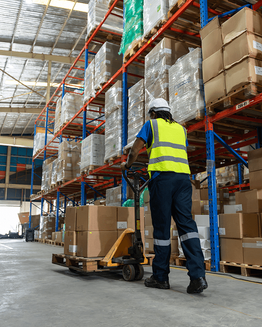 Worker moving boxes with a hand truck in a distribution center warehouse.