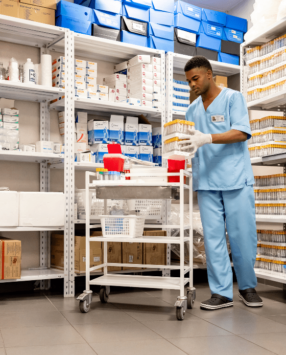 A healthcare worker organizes medical supplies on a rolling cart inside a well-stocked medical equipment storage room.