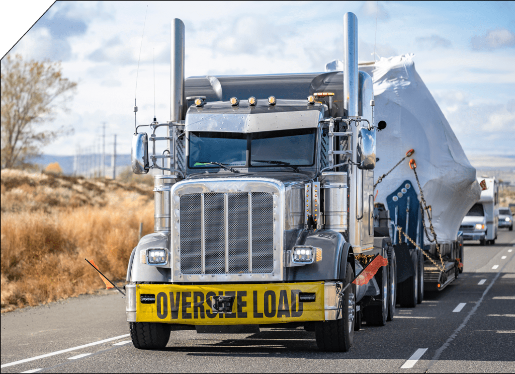 Heavy-duty truck transporting an oversized load on a highway, marked with an “Oversize Load” banner.